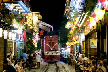 Night scene at Hanoi Train Street with a passing train surrounded by lively cafés and lantern-lit storefronts, capturing one of Vietnam’s most iconic urban experiences.