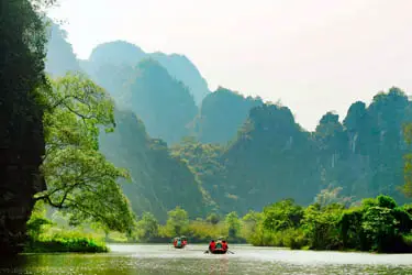 Small boats drifting along a tranquil river in Ninh Binh, Vietnam, surrounded by towering limestone cliffs and lush greenery often called “Ha Long Bay on land.”