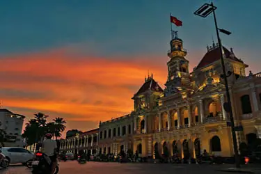 Ho Chi Minh City People’s Committee Building (Saigon City Hall) at sunset, Vietnam, with colonial-era architecture illuminated against a dramatic orange sky.