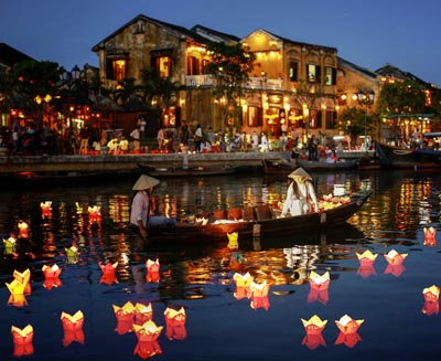 Traditional lantern boat floating on the Thu Bon River in Hoi An Ancient Town, Vietnam, with glowing paper lanterns reflecting on the water and historic riverside buildings illuminated at night.