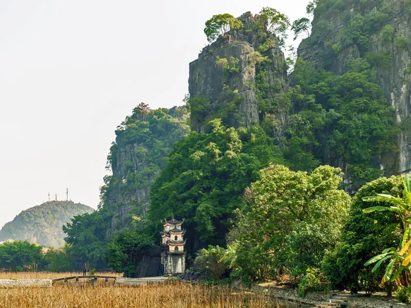 Ancient pagoda nestled beneath towering limestone cliffs in Ninh Binh, Vietnam