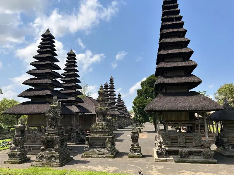 Taman Ayun Temple complex with iconic thatched-roof pagodas and intricately carved shrines set against tropical greenery in Bali.