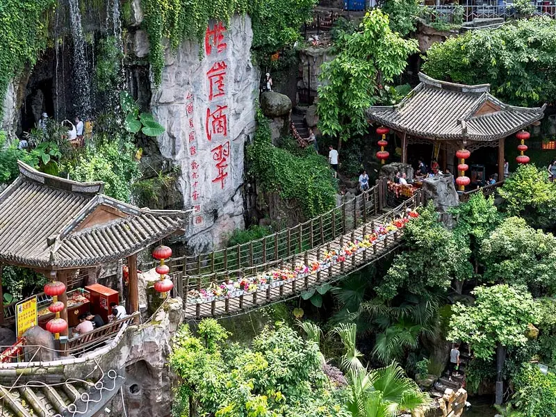 Hanging bridge at Hongya Cave in Chongqing with traditional Chinese pavilions, red lanterns, and lush greenery above cliffside waterfall