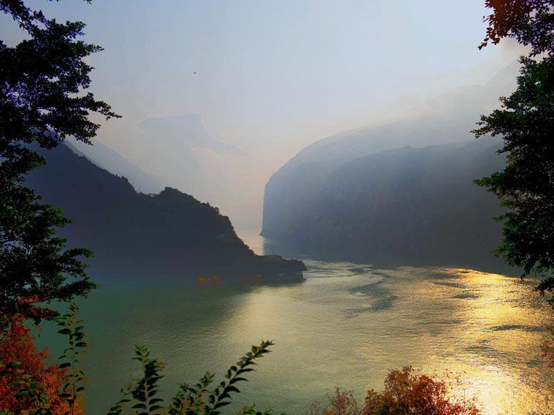Sunlit misty cliffs of the Yangtze River Three Gorges at dawn with golden reflections on the water in China