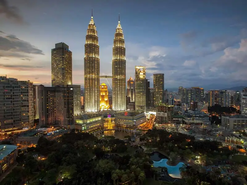 Evening skyline of Kuala Lumpur with the Petronas Twin Towers illuminated above KLCC Park.