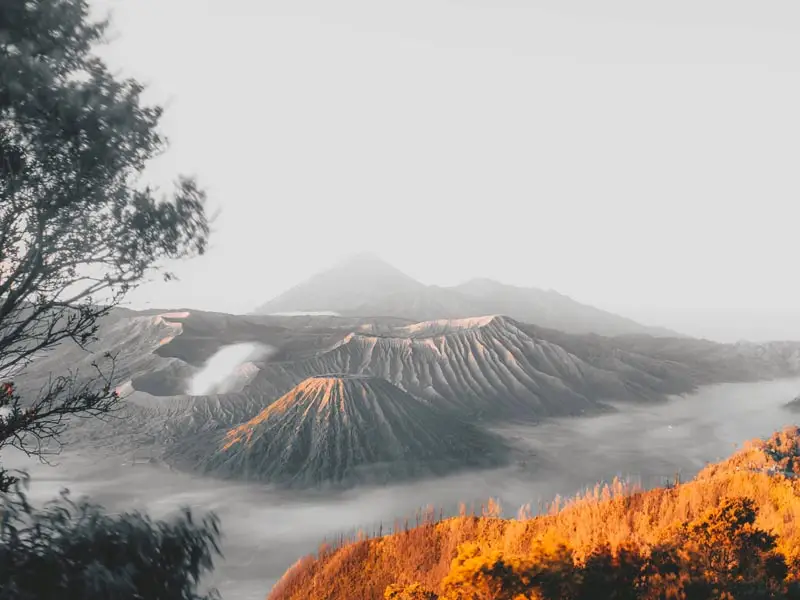 Panoramic Mount Bromo crater system wrapped in low-lying cloud and warm sunrise light across the sacred Tengger highlands of Indonesia