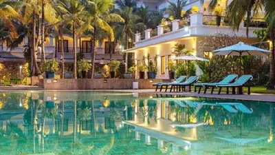 Lotus Blanc Resort Siem Reap swimming pool at dusk, luxury boutique hotel near Angkor Wat with palm-lined courtyard and elegant Khmer-inspired architecture.