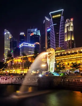 Night view of the Merlion Park in Singapore, featuring the iconic statue and modern skyline along Marina Bay.
