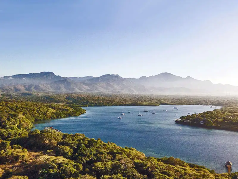 West Bali rainforest coastline meeting open lagoon waters with volcanic backdrops on the horizon, showcasing the secluded character of northwest Bali
