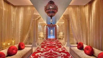 Opulent corridor at ITC Mughal, Agra, featuring ornate red carpet, draped golden curtains, carved columns, and a decorative hanging lantern leading toward a grand archway.