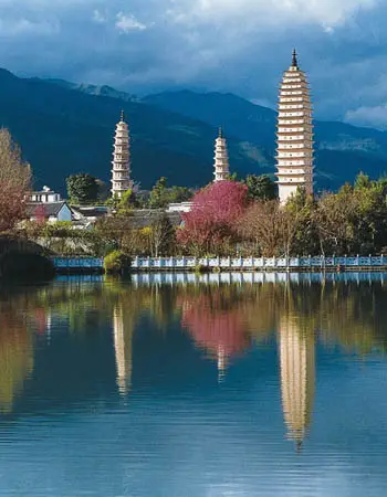 Three Pagodas of Chongsheng Temple in Dali reflected on a calm lake, with Cangshan Mountains rising behind this iconic Yunnan landmark.