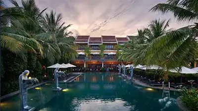 Swimming pool surrounded by tropical palms at La Siesta Hoi An Resort in Hoi An, Vietnam, a boutique luxury hotel near the UNESCO-listed Hoi An Ancient Town.