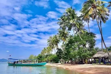 Kep Beach in Kep, Cambodia, with palm-lined shoreline and traditional fishing boat along the Gulf of Thailand—peaceful coastal destination near Kep National Park.