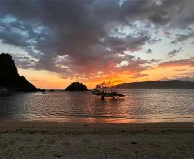 Sunset over a tranquil beach in Lombok, Indonesia, with calm waters, silhouetted islands, and vibrant evening skies along the island’s scenic coastline.