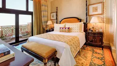Luxurious guest room at The Leela Palace, New Delhi, featuring a king bed with ornate headboard, and a balcony with city views, perfect accommodation for any luxury India itinerary