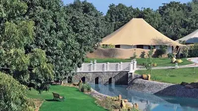 Scenic view of The Oberoi Vanyavilas Wildlife Resort, Ranthambore, featuring luxury tented accommodations set amid lush greenery, a small bridge over a water channel, and landscaped grounds.