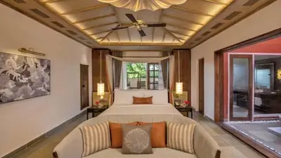 Spacious luxury tented suite at Taj Sawai Ranthambore featuring a canopy bed, elegant seating area, high vaulted ceiling, and warm ambient lighting with views of the outdoors.