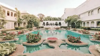 Courtyard at Taj Lake Palace, Udaipur, featuring an ornate central pool with floral planters, arched colonnades, and elegant white palace architecture.