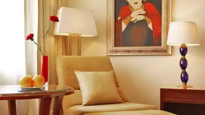 Cozy seating area at Taj Ganges, Varanasi, featuring an upholstered armchair, side table with decor, warm lighting, and framed artwork on the wall.