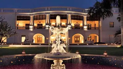 Evening view of Taj Nadesar Palace, Varanasi, featuring a grand heritage façade with arched verandas, warm lighting, and a central fountain in the foreground.
