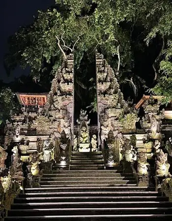 Illuminated temple-style entrance to a cultural dance venue in Ubud, Bali, featuring intricate stone carvings and traditional Balinese architecture at night.