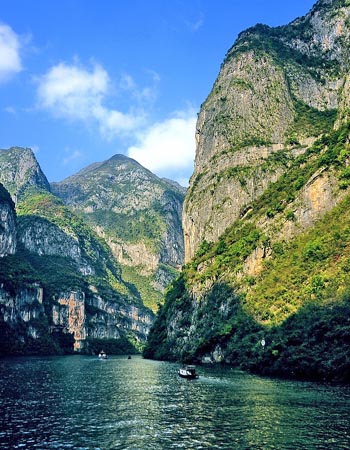 Yangtze River cruising through the Three Gorges, framed by towering limestone cliffs and dramatic mountain scenery.
