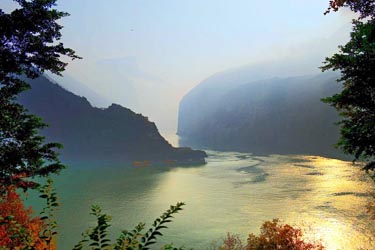 Golden sunset over the Yangtze River in China, with misty mountain silhouettes and tranquil waters reflecting warm evening light in the Three Gorges region.