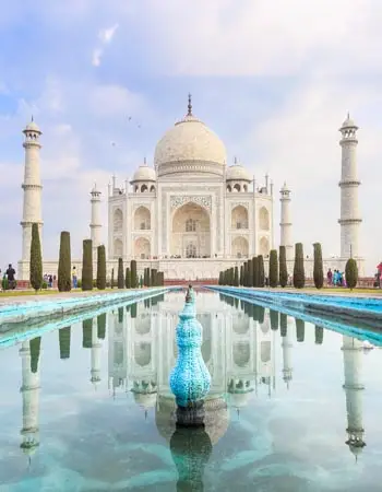Majestic front view of the Taj Mahal in Agra, India, with its white marble dome, minarets, and reflection in the symmetrical pool under a partly cloudy sky.