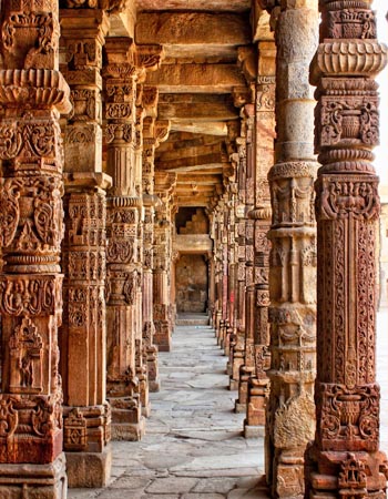 Intricately carved stone pillars lining a historic colonnade at Qutub Minar complex in Delhi, showcasing detailed geometric and floral patterns.