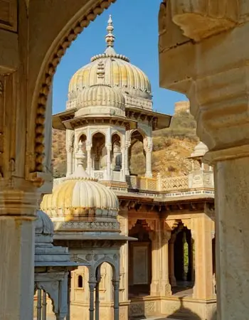 Close-up view of intricately carved domes and arches at Gaitor Ki Chhatriyan in Jaipur, India, with a backdrop of rugged hills under a clear blue sky.