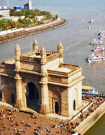 Aerial view of the Gateway of India in Mumbai, India, with crowds of tourists and boats docked along the Arabian Sea waterfront.