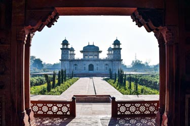 Framed view of Itimad-ud-Daulah’s Tomb in Agra, India, showcasing Mughal architecture with manicured gardens and intricate archway details in the foreground.