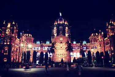 Illuminated night view of Chhatrapati Shivaji Maharaj Terminus in Mumbai, India, showcasing its stunning Victorian Gothic architecture with colorful lighting.