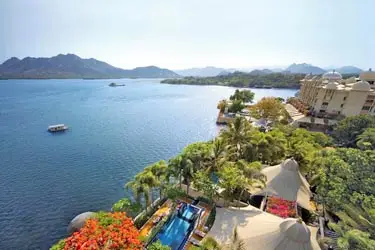 Aerial view of Udaipur’s Lake Pichola, with palace-style hotels along the shoreline, lush gardens, and hills surrounding the serene blue waters.