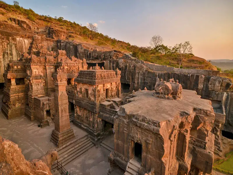 erial view of the ancient Kailasa Temple at Ellora Caves in Maharashtra, India, carved entirely from a single rock cliff and illuminated by the warm glow of sunset.
