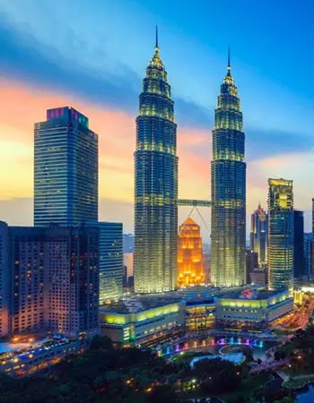 Evening skyline of Kuala Lumpur with the Petronas Twin Towers illuminated above KLCC Park.