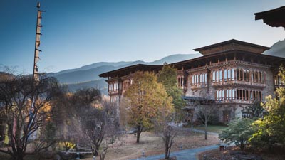 Zhiwa Ling Heritage Hotel in Paro, Bhutan, featuring traditional Bhutanese architecture set amid landscaped grounds with mountain views at dusk.