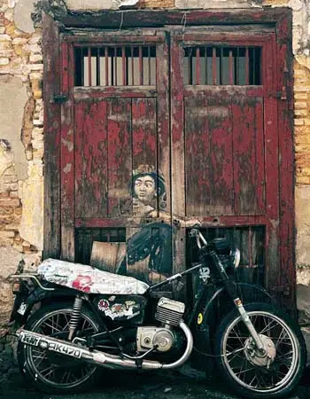 Vintage motorcycle parked against weathered heritage doors in Penang, reflecting street culture on a Penang Food Tour