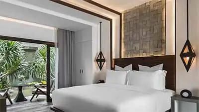 Jaya House River Park hotel room in Siem Reap, Cambodia, featuring a king bed with modern Khmer design, warm wood accents, and a private balcony overlooking tropical gardens.