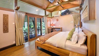River-view chalet interior at Sukau Rainforest Lodge in Sabah, Malaysia, featuring wooden furnishings and private balcony overlooking the Kinabatangan River rainforest
