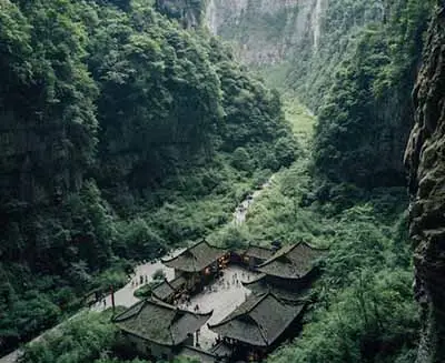Ancient temple complex nestled within a dramatic forested canyon in China, surrounded by towering cliffs and lush green mountains in a remote scenic valley.