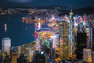 Nighttime skyline of Hong Kong Island with illuminated skyscrapers overlooking Victoria Harbour and Kowloon, showcasing modern city lights and harborfront architecture.