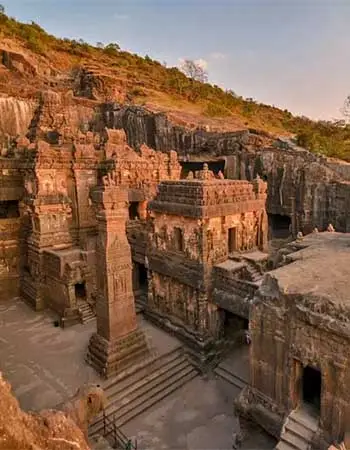 Ancient rock-cut temples at Ellora Caves in Maharashtra, India, featuring intricately carved stone structures set into a rugged hillside at sunset.