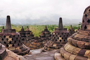 Stone stupas at Borobudur Temple in Yogyakarta, Indonesia, overlooking misty volcanic landscapes at sunrise in one of the world’s largest Buddhist monuments.