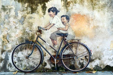 Penang street art mural of two children riding a bicycle on a weathered wall in George Town, Malaysia, a popular cultural attraction and photography spot