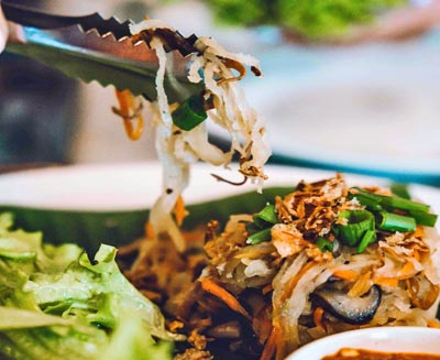 Malaysian street food being served at a local hawker stall, featuring stir-fried rice noodles with vegetables and fresh herbs