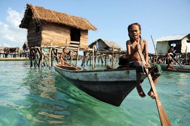 Bajau child paddling a wooden boat in a stilt village over clear turquoise waters in Sabah, Malaysia, showcasing traditional sea nomad life