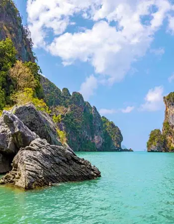 Emerald-green waters surrounded by towering limestone cliffs in Krabi, Thailand, with dramatic rock formations rising from the Andaman Sea under a bright blue sky.