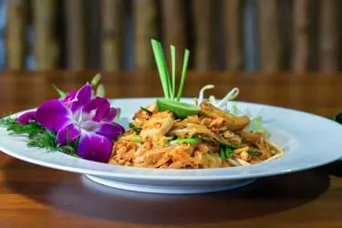 Thai-style stir-fried noodles garnished with fresh herbs and purple orchid, part of a Thai Culinary journey.