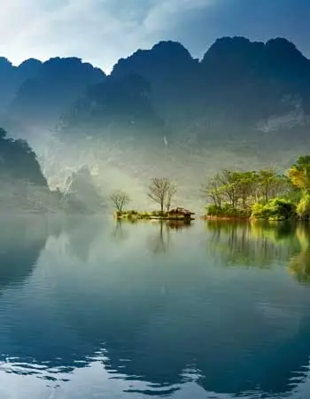 Tranquil lake surrounded by misty limestone mountains in Ninh Binh, Vietnam, capturing the region’s serene landscapes often referred to as “Ha Long Bay on land.”